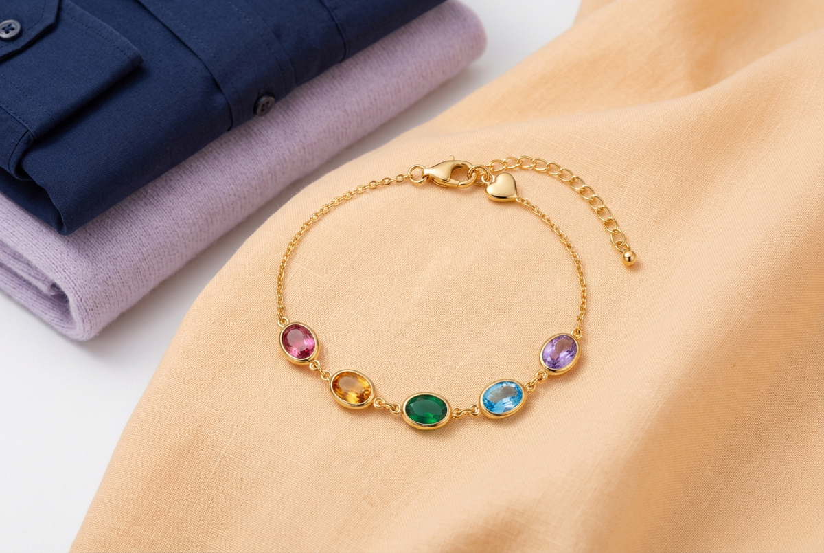 Five-color bracelet on peach cloth beside folded navy and lavender clothing