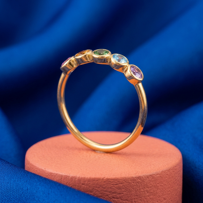 Five-color ring on coral pedestal against cobalt fabric