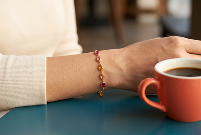Warm-colored bracelet worn at the wrist beside a coral coffee cup