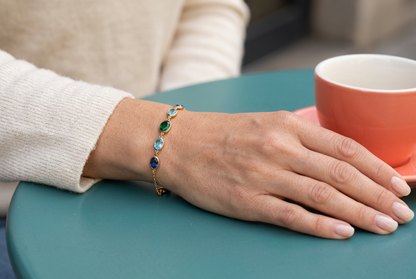 Ocean Muse bracelet worn on wrist with ivory sleeve beside coral cup on teal table